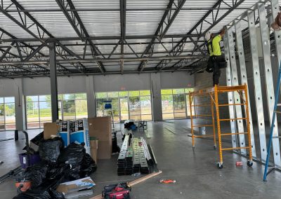 A construction worker from Commercial Builders, MD, skillfully maneuvers on scaffolding to install beams in an open indoor space. In Rockville, tools and materials are strategically scattered around as the project takes shape with precision.