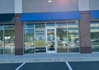 Storefront with a blue awning and a "Retail Lease Available Now" sign on the glass door, nestled in a sunny parking lot designed by Nextt Commercial Builders.