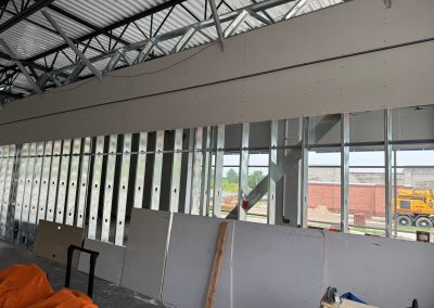 At a bustling Rockville construction site, metal framing stands sturdy with drywall partially installed. In the foreground, an orange tarp waves gently, showcasing the craftsmanship of Nextt Commercial Builders in MD.